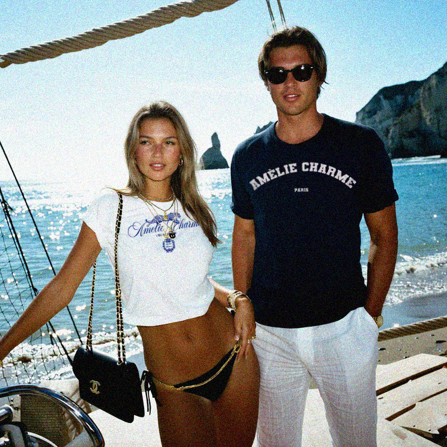 Two people standing on a boat with a scenic beach and cliffs in the background